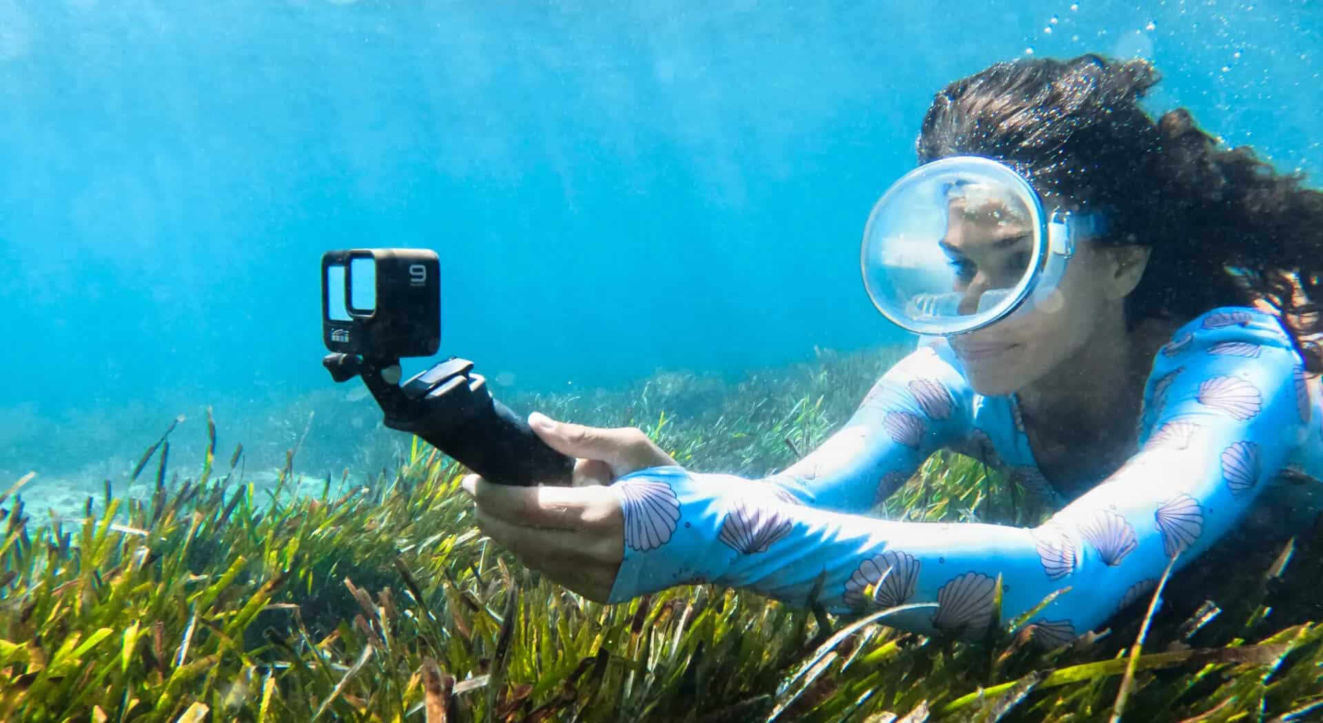 A woman in a blue wetsuit is using an underwater camera.