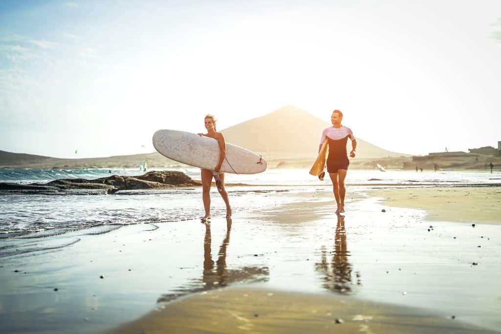 couple-surfers-running-on-beach