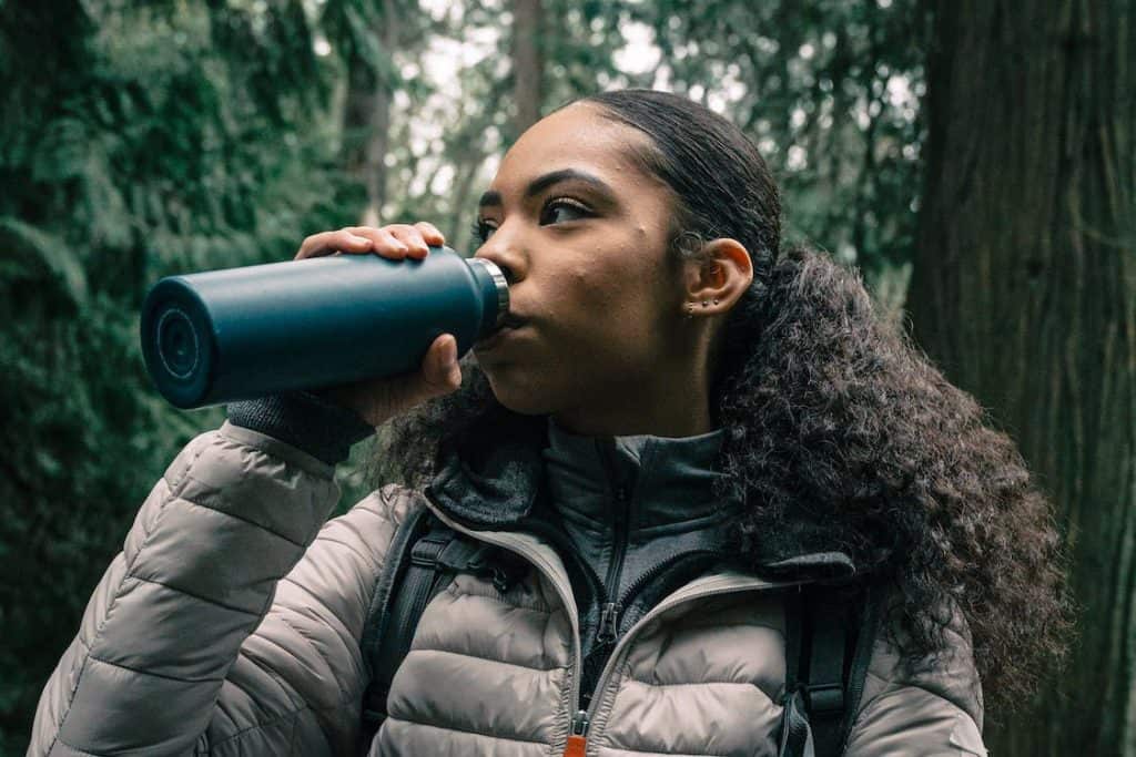 A woman drinking from the Best insulated water bottle in the woods.