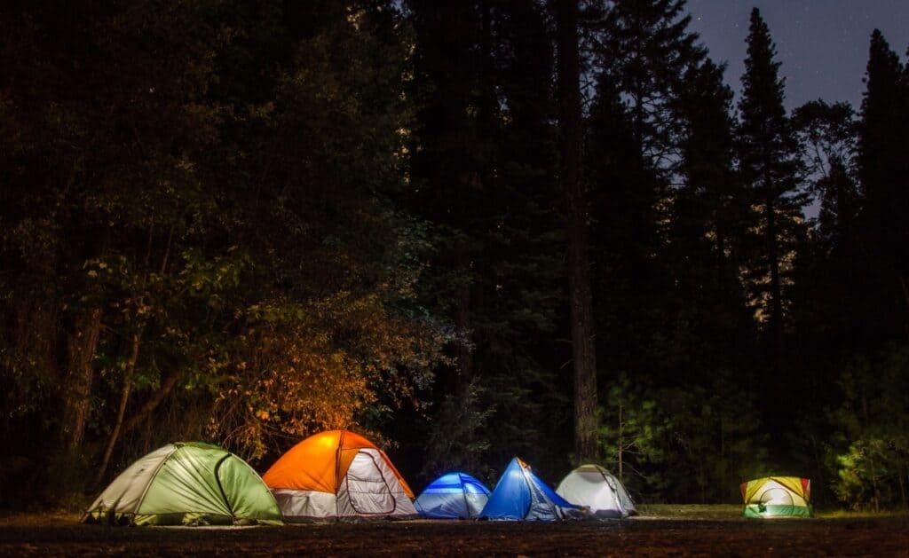 A group of tents illuminated at night in a wooded area, suitable for camping.